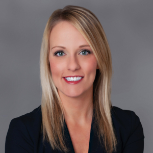 With shoulder-length blond hair and a black suit, attorney, Amanda Crain, sits for a professional portrait in a studio setting.