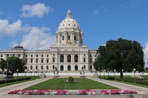 A photo of Minnesota's capital on a sunny day. The dome sits centered in front of colorful landscaping. 