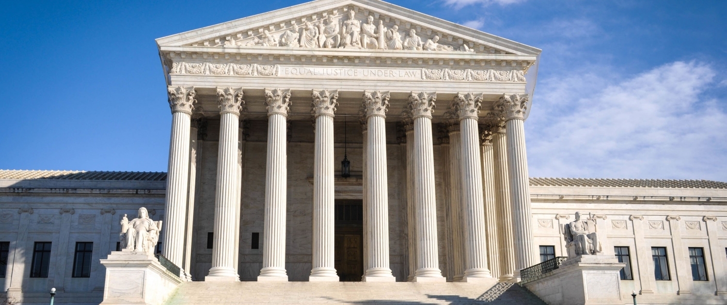 Close cropped photo of the Supreme Court pillars. Sunny clouds frame the bas relief and the text etched into the stone reading "Equal Justice Under Law."