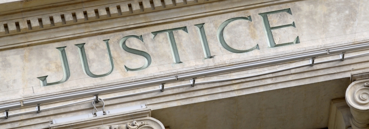 A close cropped photo of the word "Justice" etched into the marble facade of a building. 