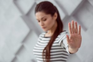 A woman in a black and white striped shirt looks down while holding out her hand with her palm outward in a gesture of "stop."