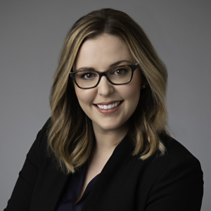 Close-cropped portrait of Amy Boyle, attorney. Sitting at an angle in front of a studio setting, she smiles confidently at the camera. 