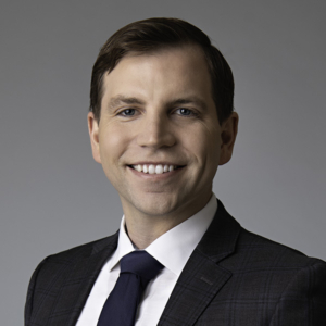 Closely-cropped photo of attorney Nathaniel Smith. He smiles at the camera, wearing a gray suit and sitting in a studio setting.