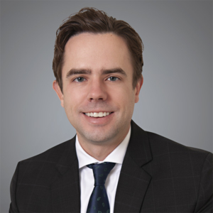 Attorney, Ross Stadheim sits in a studio setting and smiles at the camera while wearing a professional suit. 