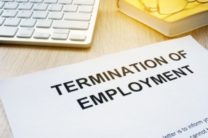 A sheet of paper reading "termination of employment" rests on a desk between a book and a laptop.