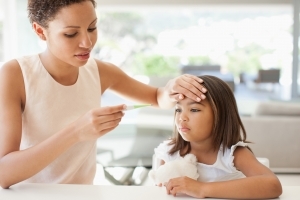 A mother checks her daughter's temperature as they sit in a clean, well-lit kitchen.