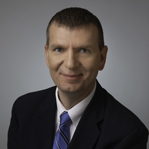 Jon Leavitt, attorney, sits for a studio portrait, wearing a black suit and smiling. 