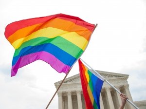 Two rainbow flags catch the breeze in front of the columns of the capitol building. 