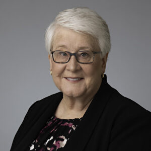 Portrait of Susan Coler, attorney, smiling at the camera while wearing a black suit and matching glasses. 