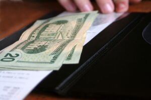 Three twenty dollar bills resting in a restaurant bill folder. 