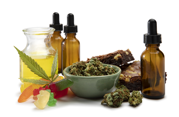Cannabis oils and bud in a small bowl surrounded by sweet edibles